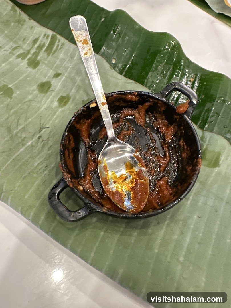 Spoon in a small dish with remnants of food on a banana leaf