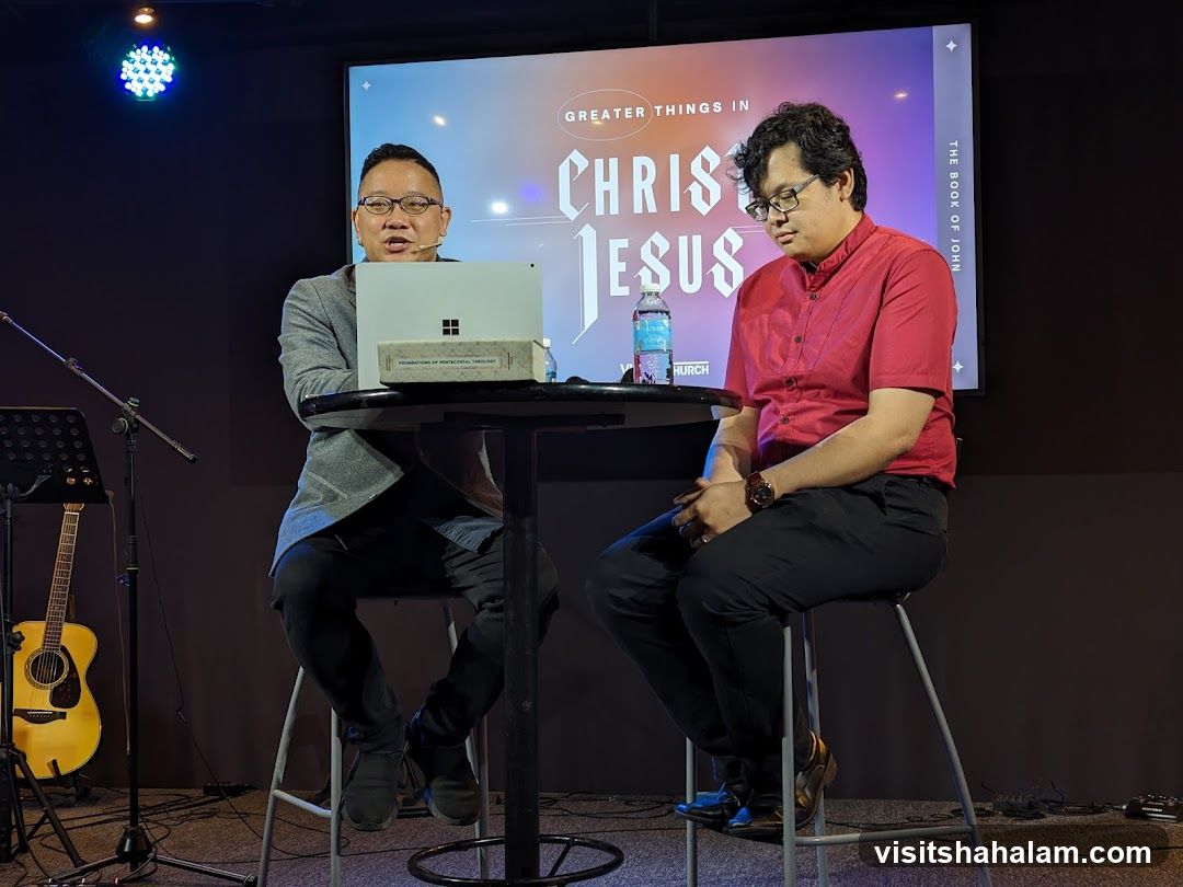 Two men sitting on stools in front of a screen