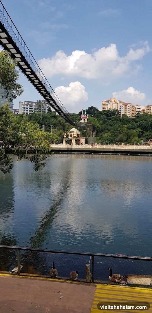 Suspension bridge over a lake with buildings and a dome structure in the background