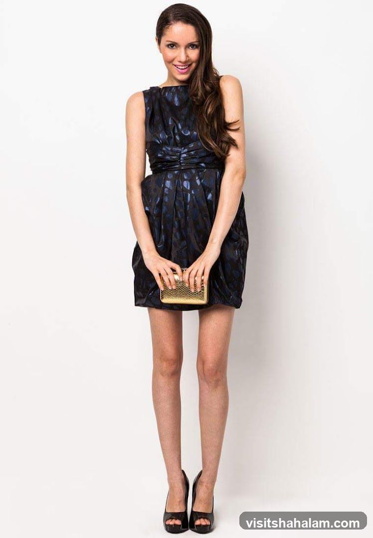 Woman in a dark patterned dress holding a gold clutch