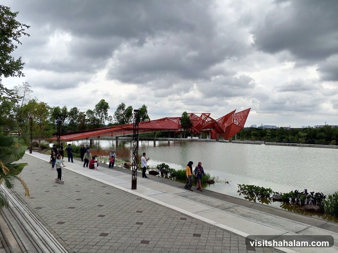 People enjoying a park with a modern red structure and a lake