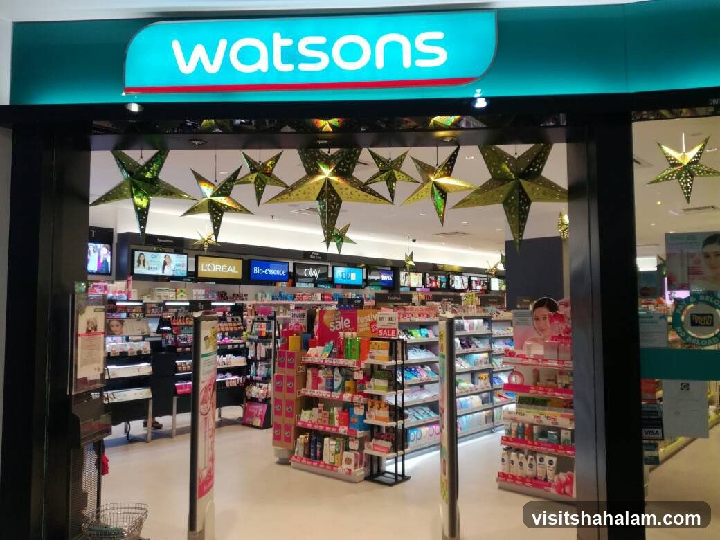 The exterior of a Watsons store is visible, with the brand's logo prominently displayed on a teal sign above the entrance. Festive star decorations hang from the ceiling inside the store. The interior is stocked with various health and beauty products, with shelves organized by brand and product type. Signs indicating "sale" are visible on some displays.