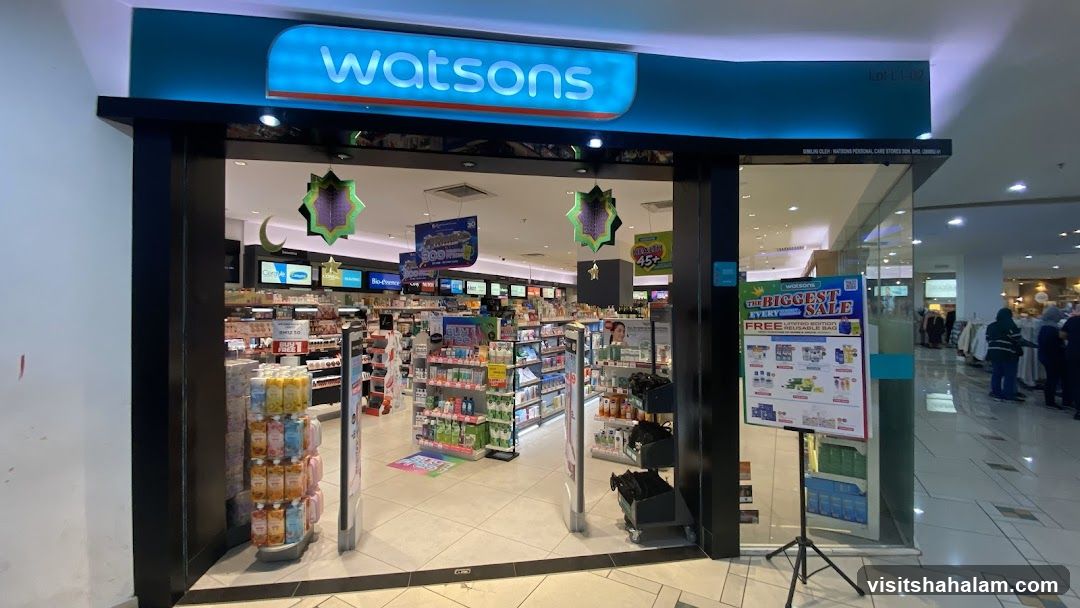 The exterior of a Watsons store is visible, with its prominent blue and white signage above the entrance. The store is well-lit and stocked with various health and beauty products. Inside, shelves are filled with items, and promotional displays are visible. A large sale poster is placed outside the entrance.