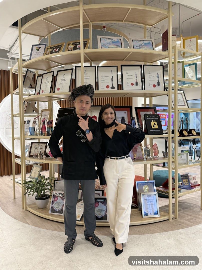 Two people posing in front of shelves filled with awards and certificates