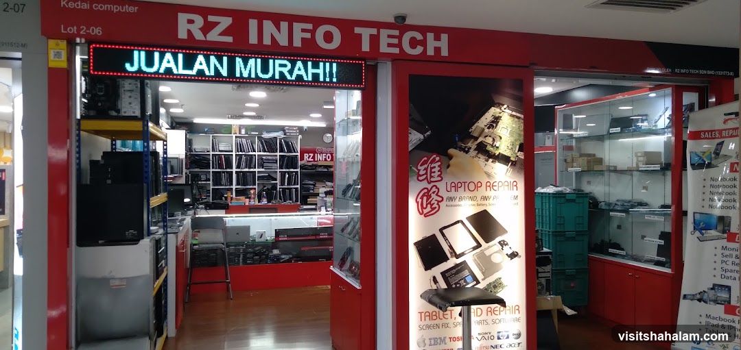 The storefront of RZ INFO TECH, a computer store. An LED sign above the entrance displays "JUALAN MURAH!!". The shop displays computers, laptops, and computer parts. A poster advertises laptop and tablet repair services.