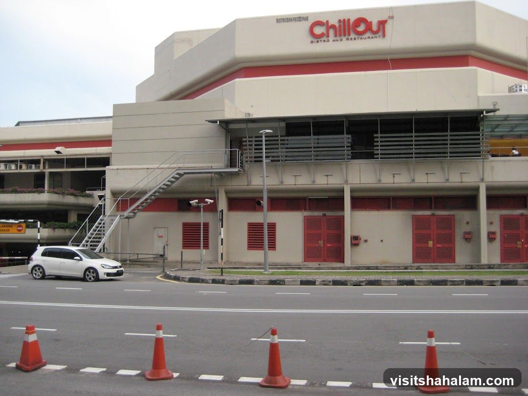 The exterior of a multi-story building with the prominent red and white sign for "ChillOut Bistro and Restaurant" visible on the upper level. The building has a modern architectural style with large windows and red doors on the lower level. An external metal staircase is visible on the left side of the building. A white car is parked on the road in front of the building.