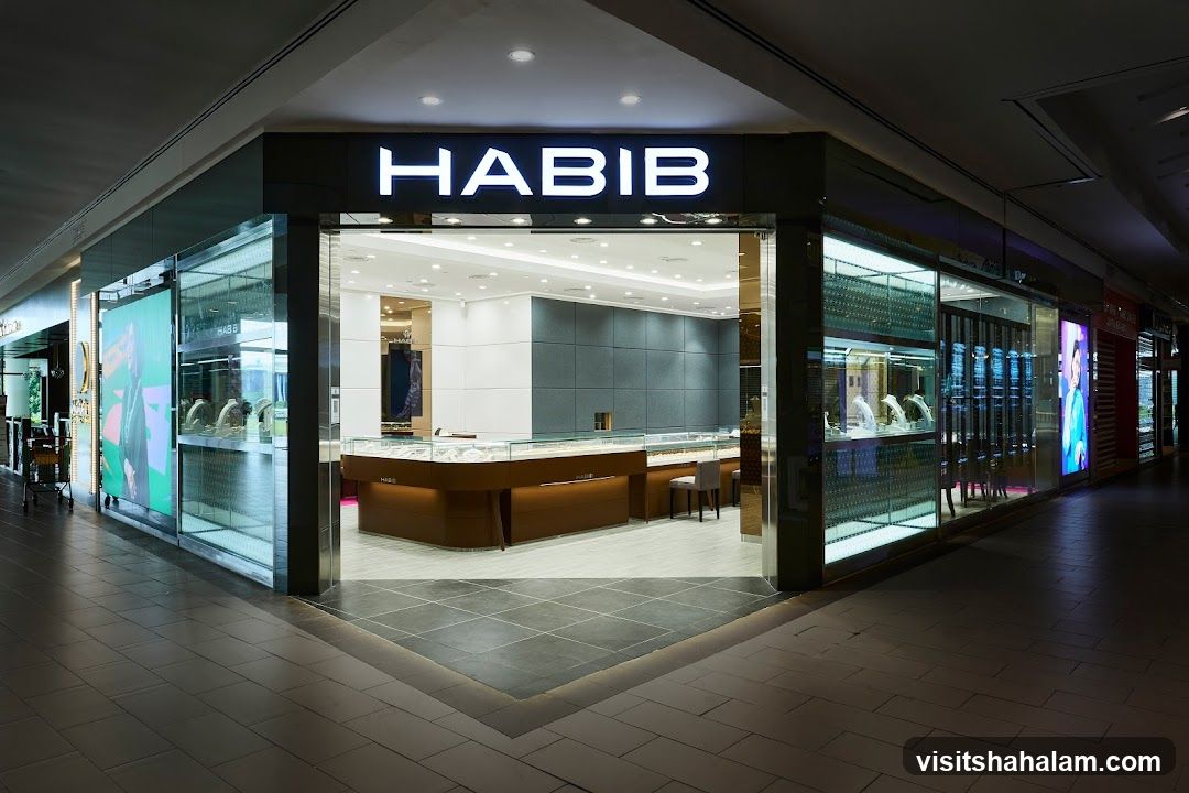 The exterior of a Habib jewelry store, with a large illuminated sign above the entrance. The storefront features large glass windows displaying jewelry inside, and a modern, well-lit interior visible through the open entrance.