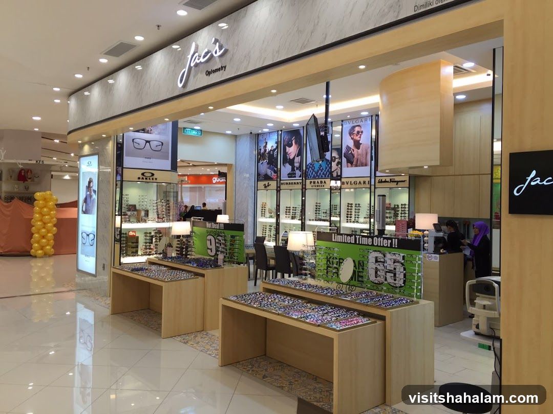 The exterior of an optometry shop with displays of eyeglasses and sunglasses. The shop's name, 'Jac's Optometry', is visible above the entrance. Promotional posters and displays of eyewear are arranged inside and outside the shop.