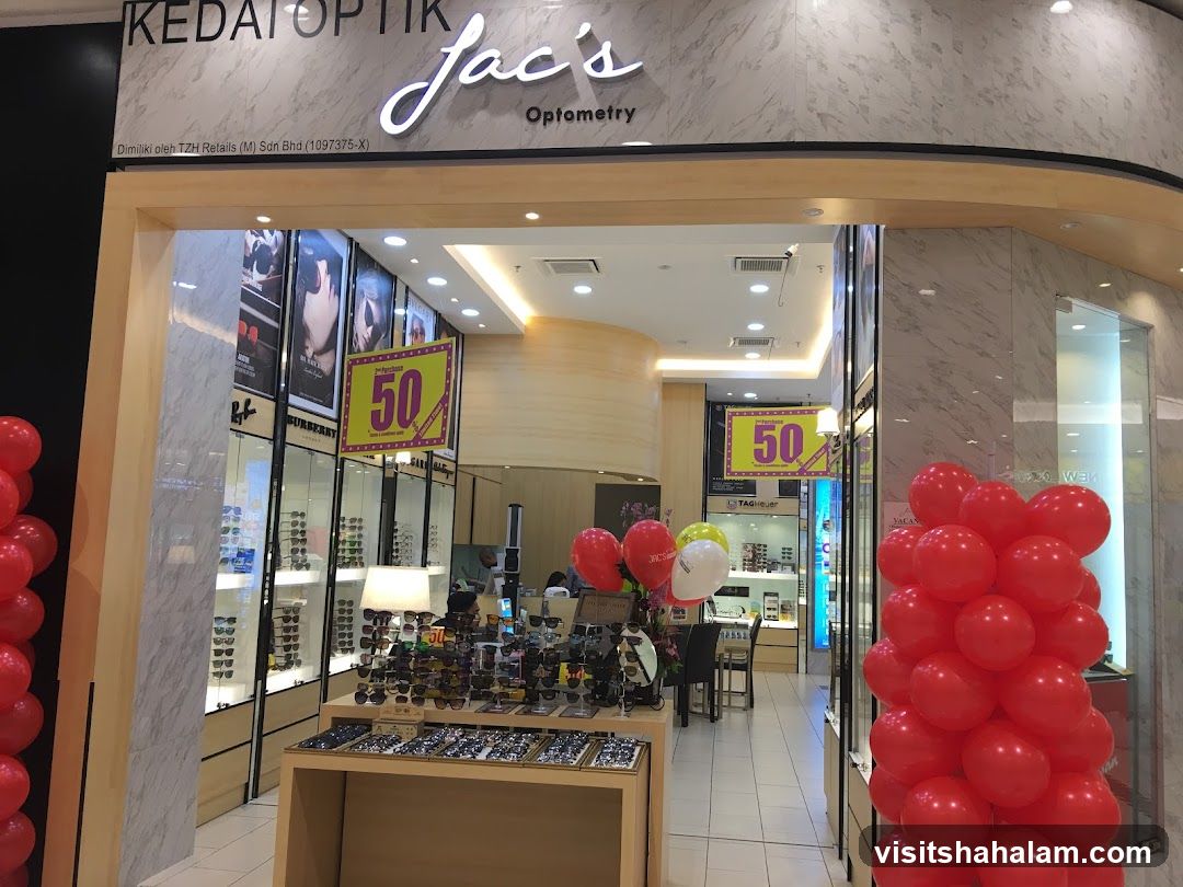The exterior of a store called Jac's Optometry. The store has a large display of eyeglasses and sunglasses. There are also promotional posters for a 50% discount. Red balloons are visible outside the store.